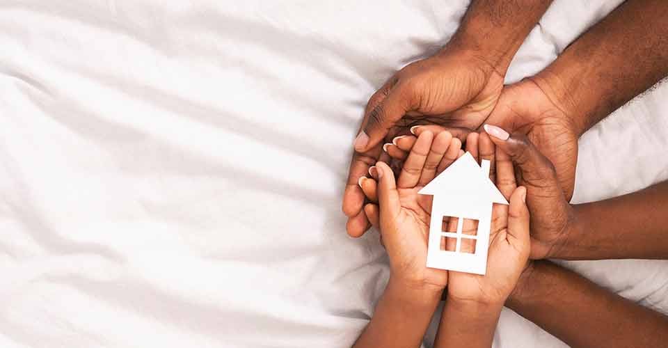 A family of three holding paper house figure in hands