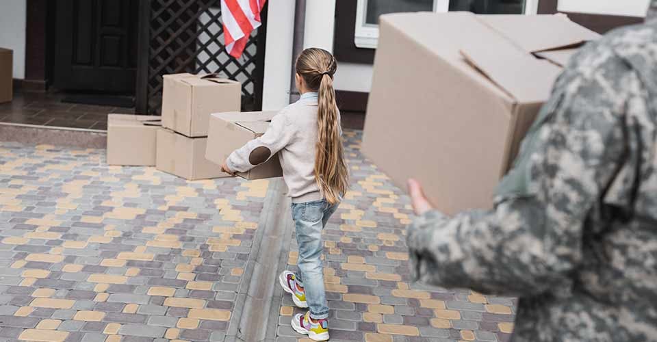 A girl carrying cardboard box to new house with military father