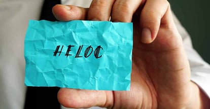 A hand holding a piece of paper with HELOC word