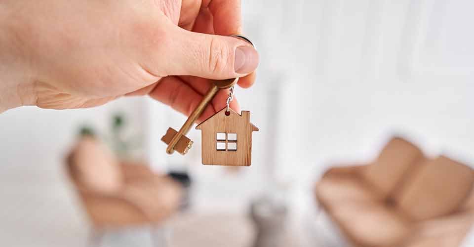 A hand holding key with house shaped keychain