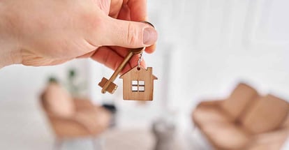 A hand holding key with house shaped keychain