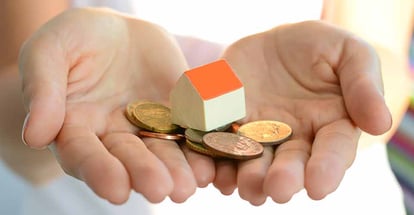 A hand holding model house and coins for down payment