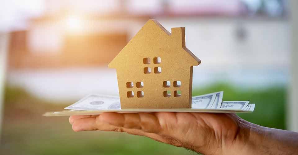 A hand holding money and model house