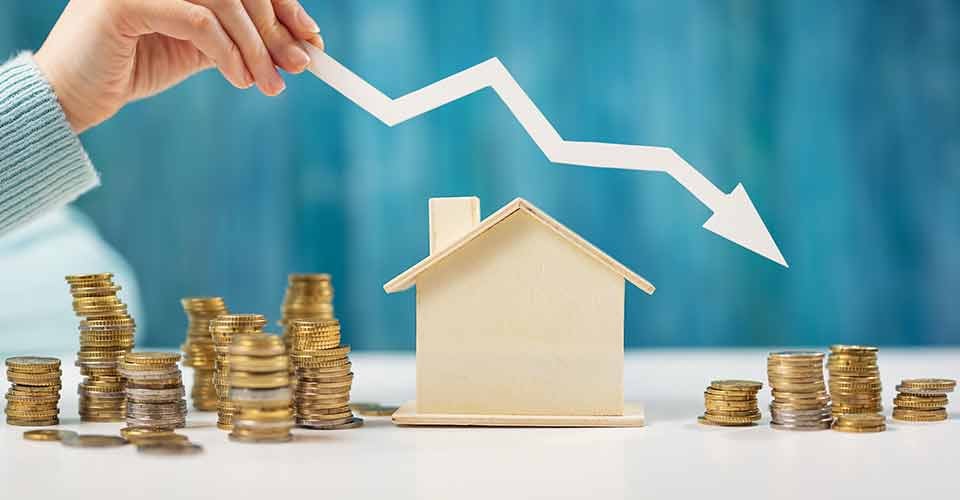 A hand holds an arrow over house model and stack of coins