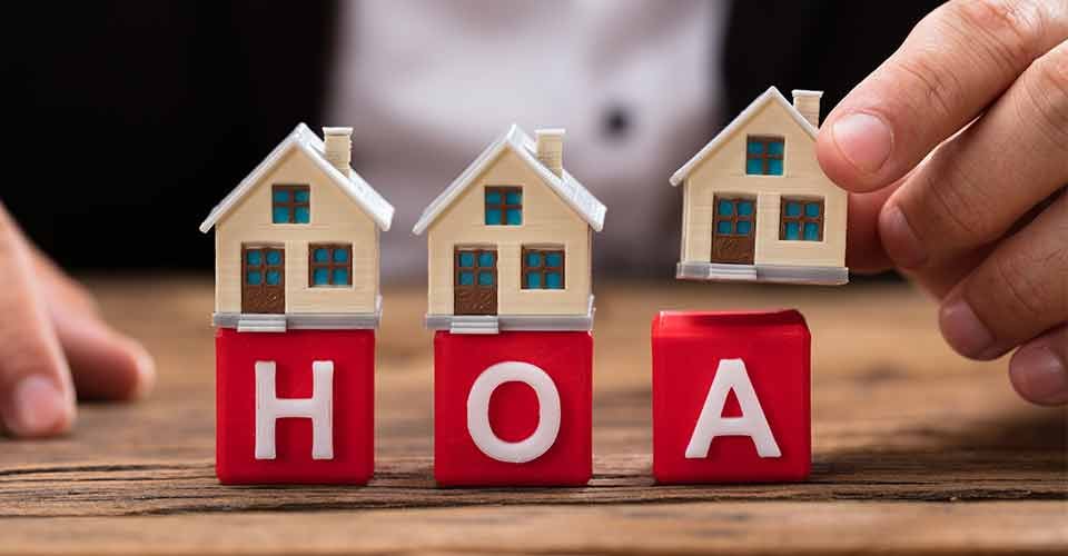 A hand placing house model over red HOA blocks on wooden desk