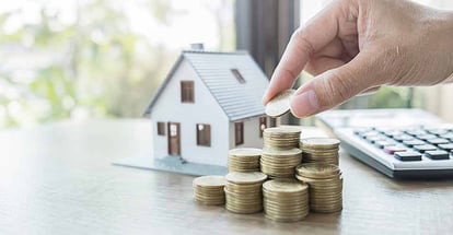 A hand putting money on coin stack and house model on table