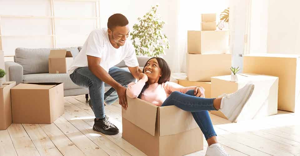 A happy black couple playing together with cardboard box in their new house