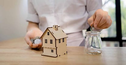 A house model and hand putting a coin on a jar