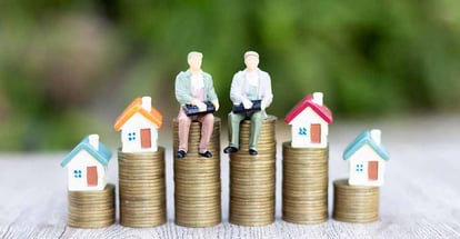 A house model and miniature home buyer figure on a pile of coins