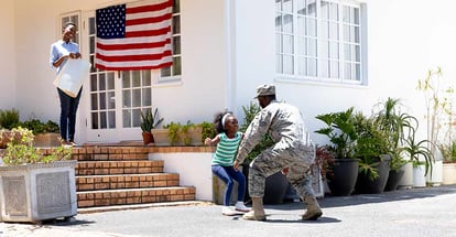 A mother and daughter welcoming a military father in their new house on a sunny day