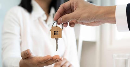 A new homeowner accepts a house key from a real estate agent