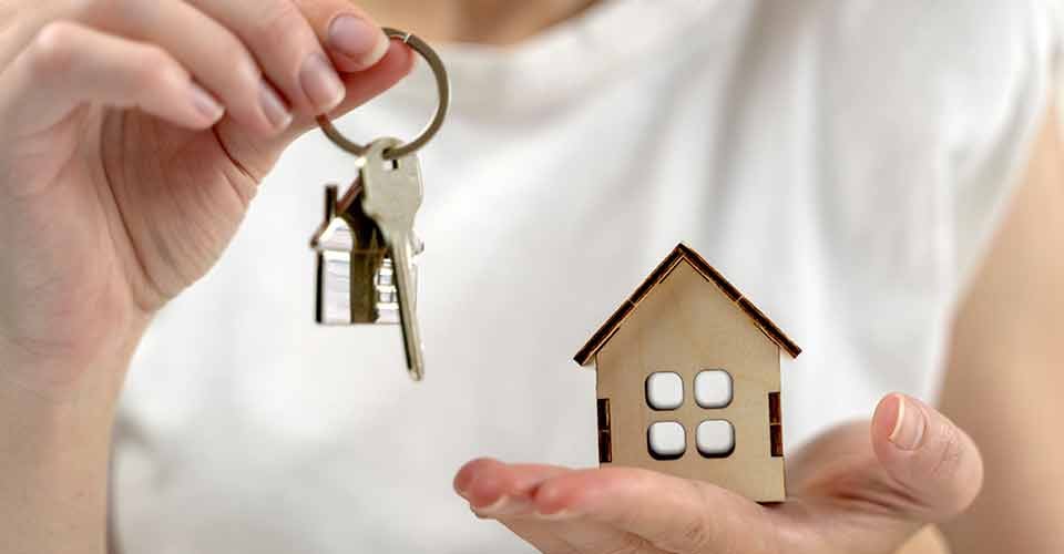 A person holding a house key and a wooden house model
