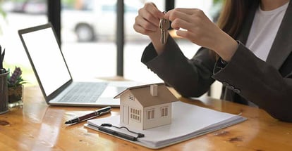 A person holding a key and house model on the table