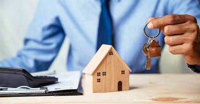 A person holding a key in front of model house on table