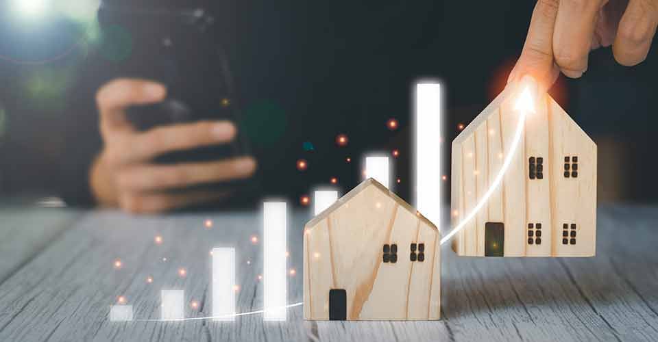 A person holding wooden model houses and virtual graph for real estate investment