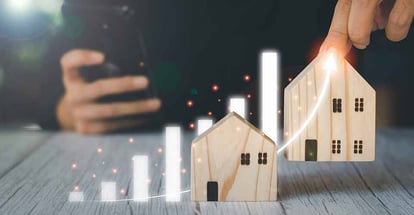 A person holding wooden model houses and virtual graph for real estate investment