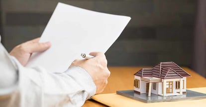 A person looking at documents for home loan with small model house on the table