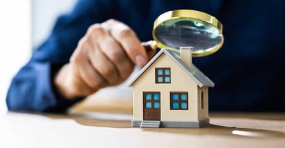 A person using magnifying glass to look at model house for appraisal and inspection