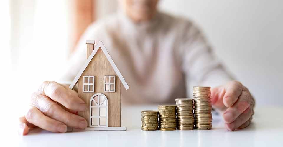 A person with coins and model house on hand for real estate investment