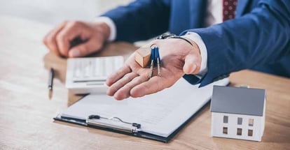 A real estate agent holding keys near house model