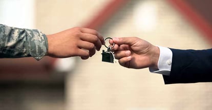 A realtor giving new house key to man in military uniform