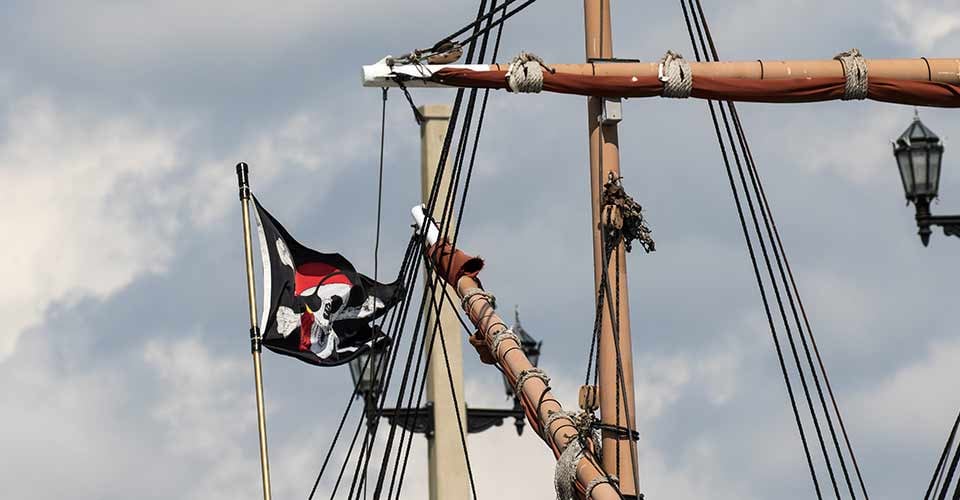 A skull and cross bones pirate flag flying from the rigging of a tall ship