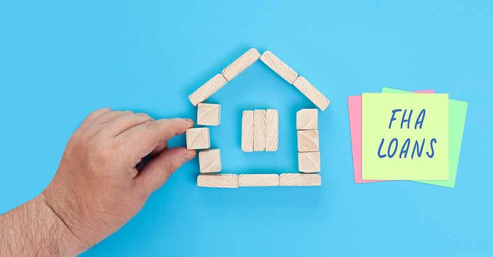A small house made of wooden blocks and colored sticky notes with the words FHA loans