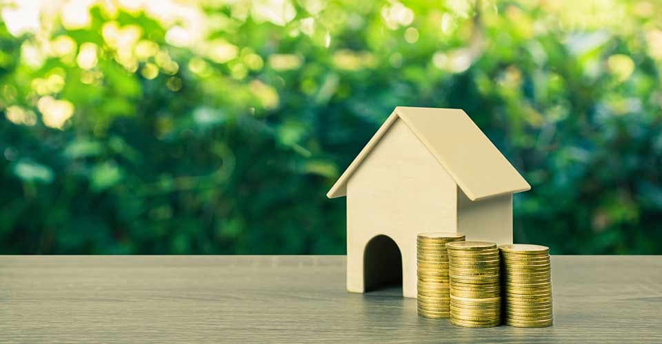 A small house model with stack of gold coins on wooden table