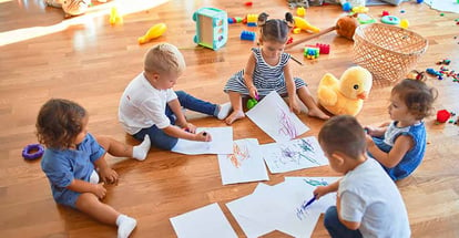Adorable group of toddlers sitting on the floor drawing at school