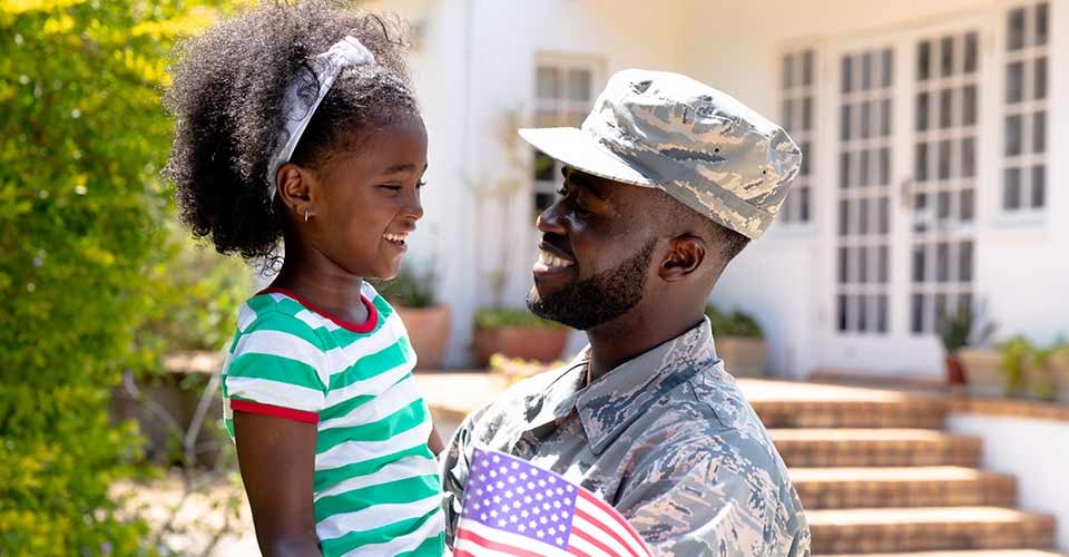 African American soldier holding his daughter and standing by the new house