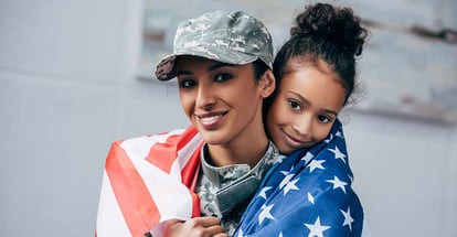 African american daughter and female soldier in military uniform wrapped with american flag at new home