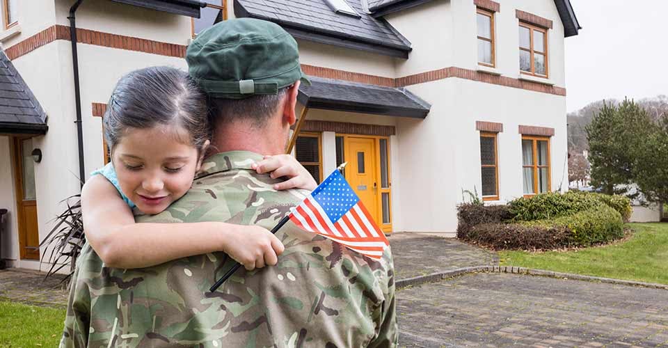 American soldier carrying girl in front of a house