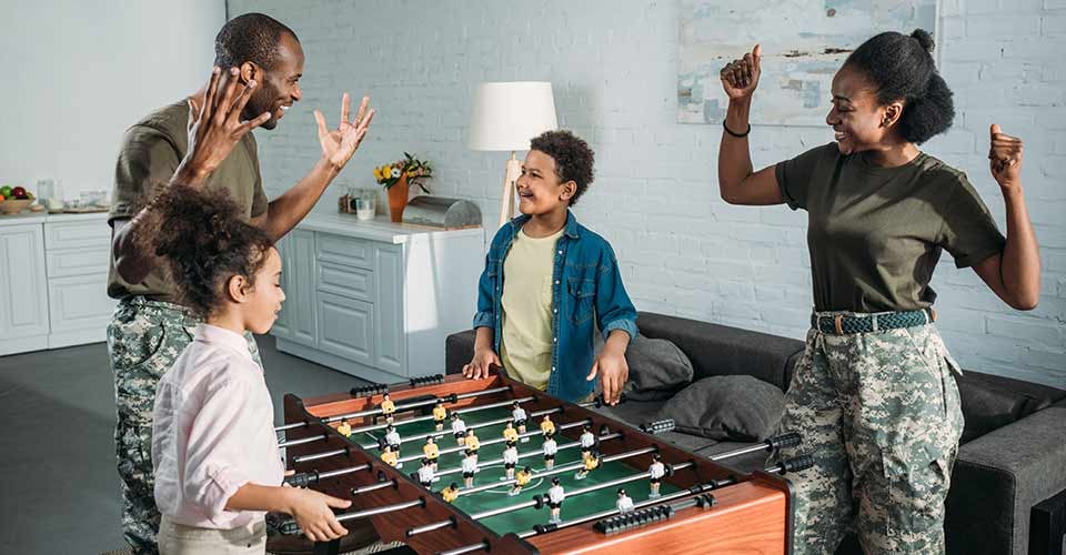 Army soldiers with happy kids playing table football on new home