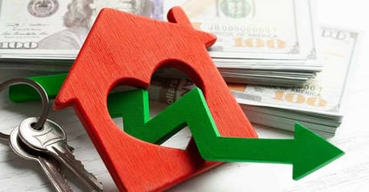 Arrow down and house with money on white wooden background