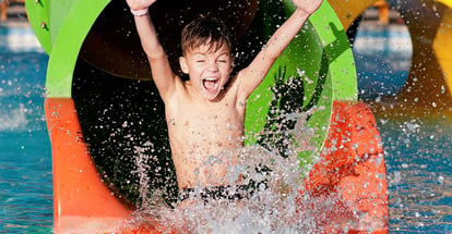 Boy in pool after going down water slide during summer