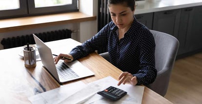Busy woman preparing annual rental income report and checking result on calculator