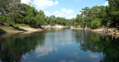 Calm river with reflections of clouds and trees in water