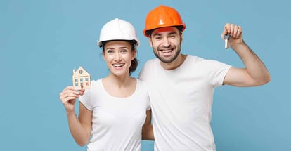 Cheerful young couple in protective helmet holding keys and ready for home renovation