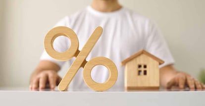 Close up of a wooden percent symbol on a table with a young man and a little house