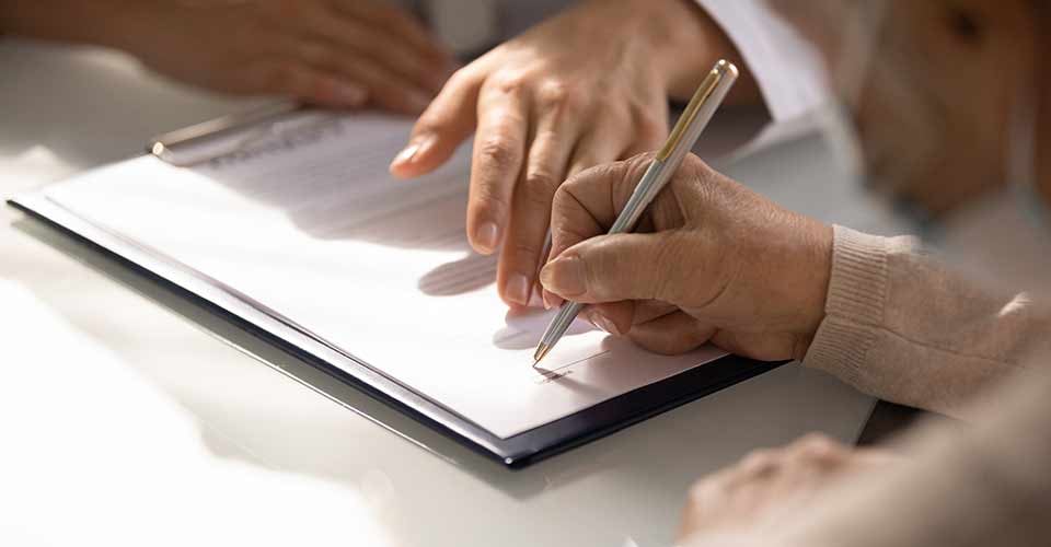 Close up of aged hand signing document at agent office