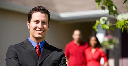 Confident Real Estate Agent With Home Sellers Behind