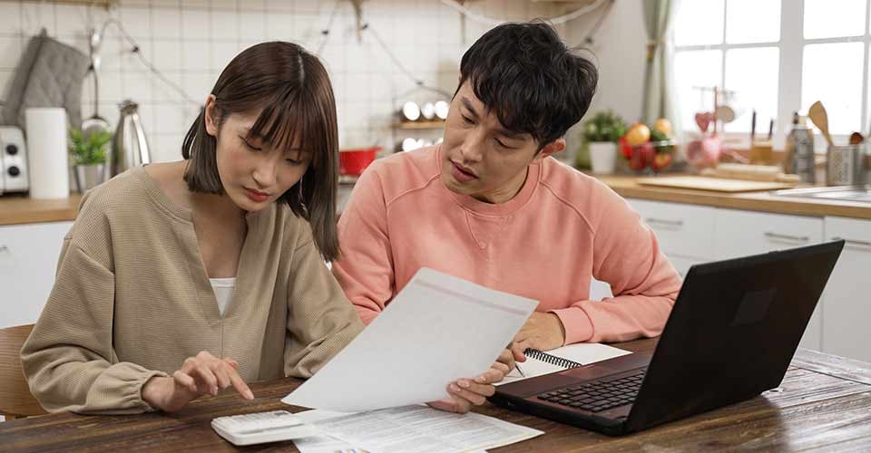 Couple calculating mortgage payment on calculator in dining room at home