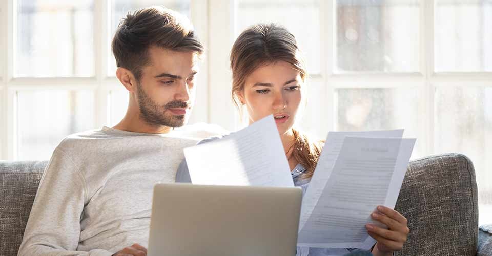 Couple sitting on couch with computer and reading mortgage documents