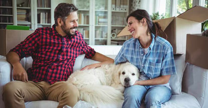 Couple sitting on sofa with their pet dog in their new house