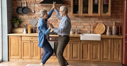 Energetic middle aged family couple dancing to music in kitchen