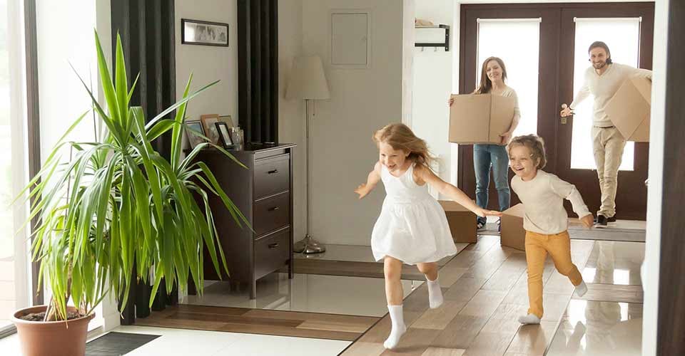 Excited children exploring home interior and parents holding cardboard boxes