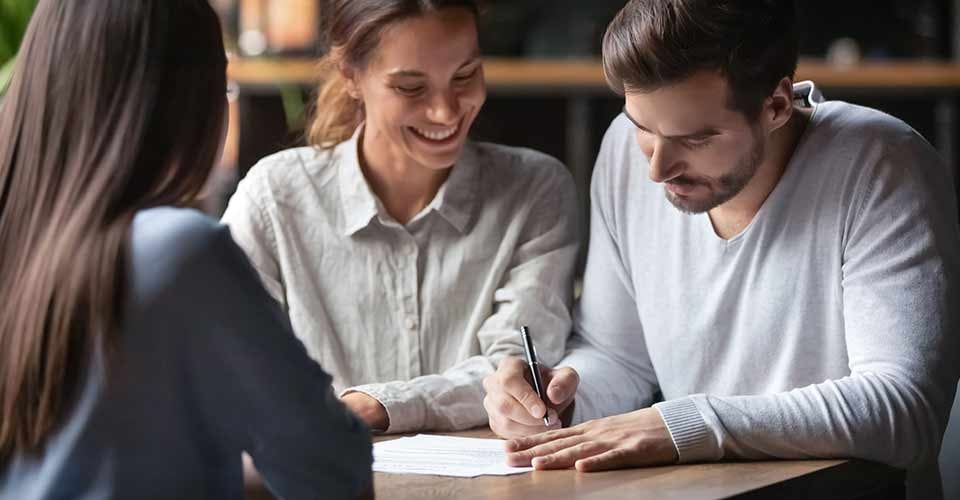 Excited couple meeting with female realtor to sign home purchase contract