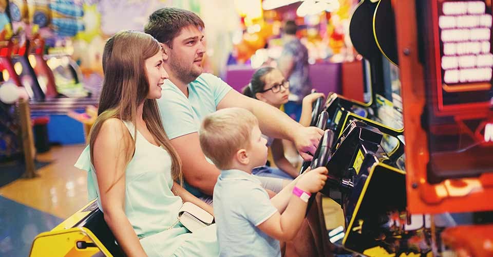 Family mother father and little boy driving car arcade in game machine at an amusement park