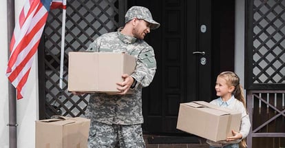 Father in military uniform and daughter holding cardboard boxes outside their new house
