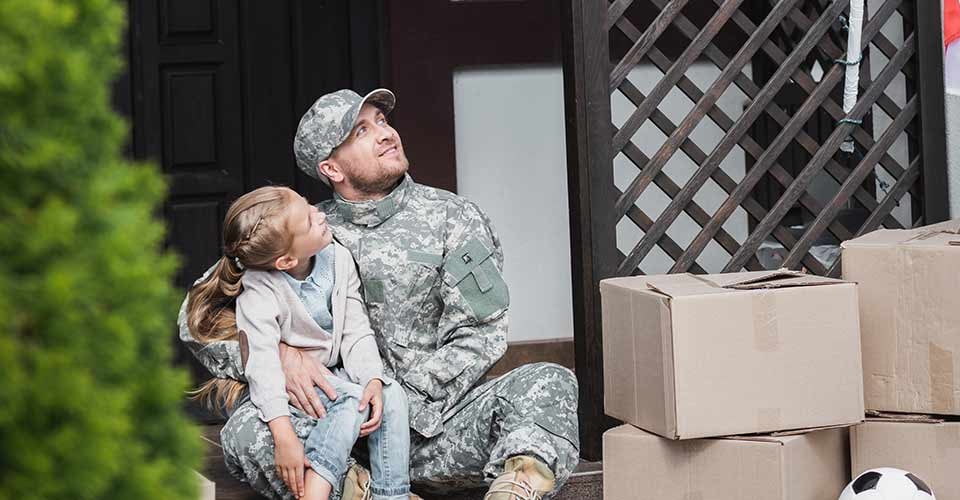 Father in military uniform hugging daughter and sitting outside their new house on moving day